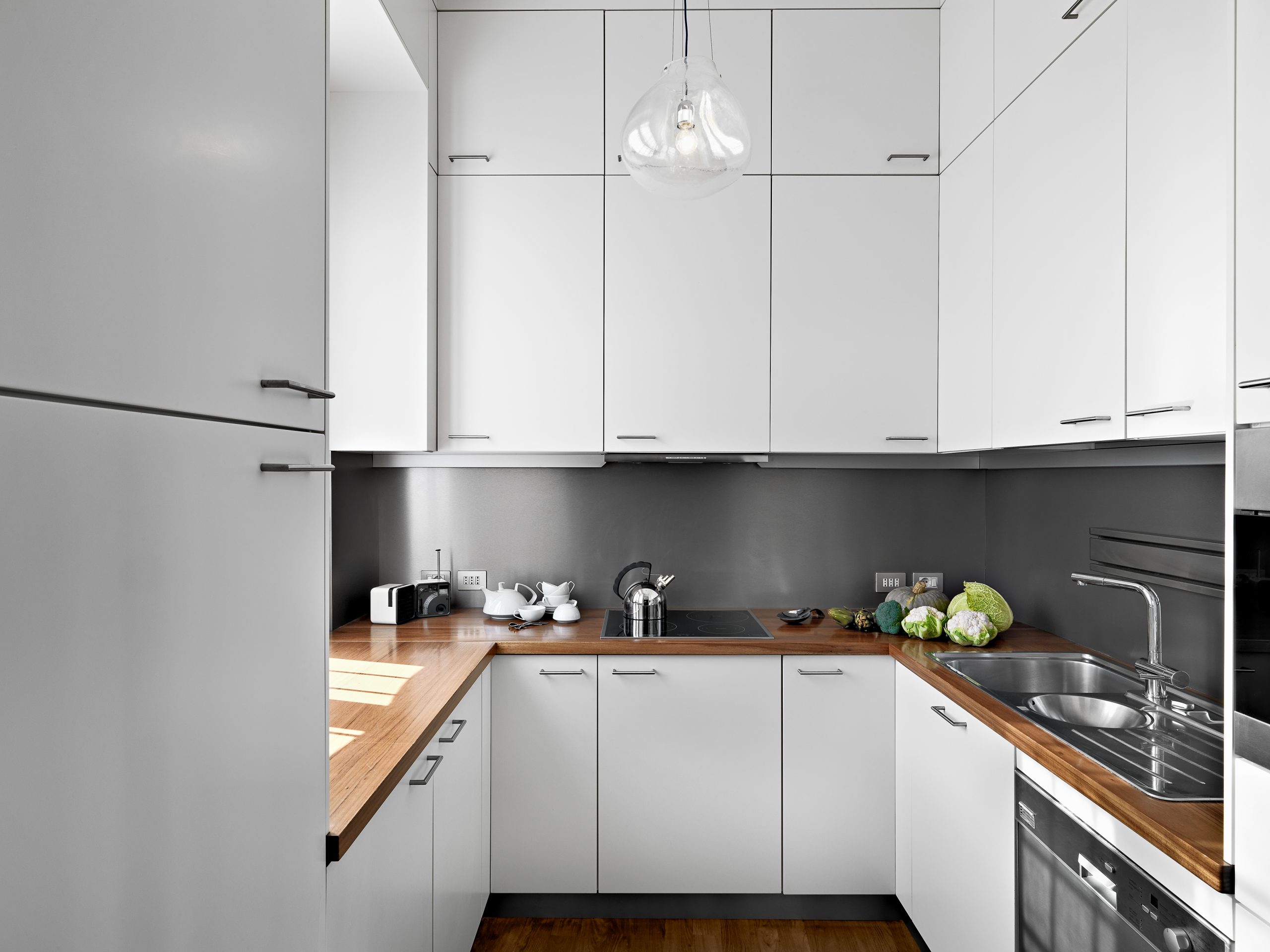 Белая глянцевая кухня с серой столешницей и фартуком в интерьере фото